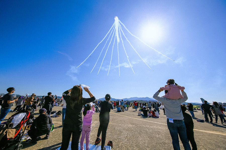 하늘에서 연기를 뿜으며 나는 항공기를 올려다보는 사람들