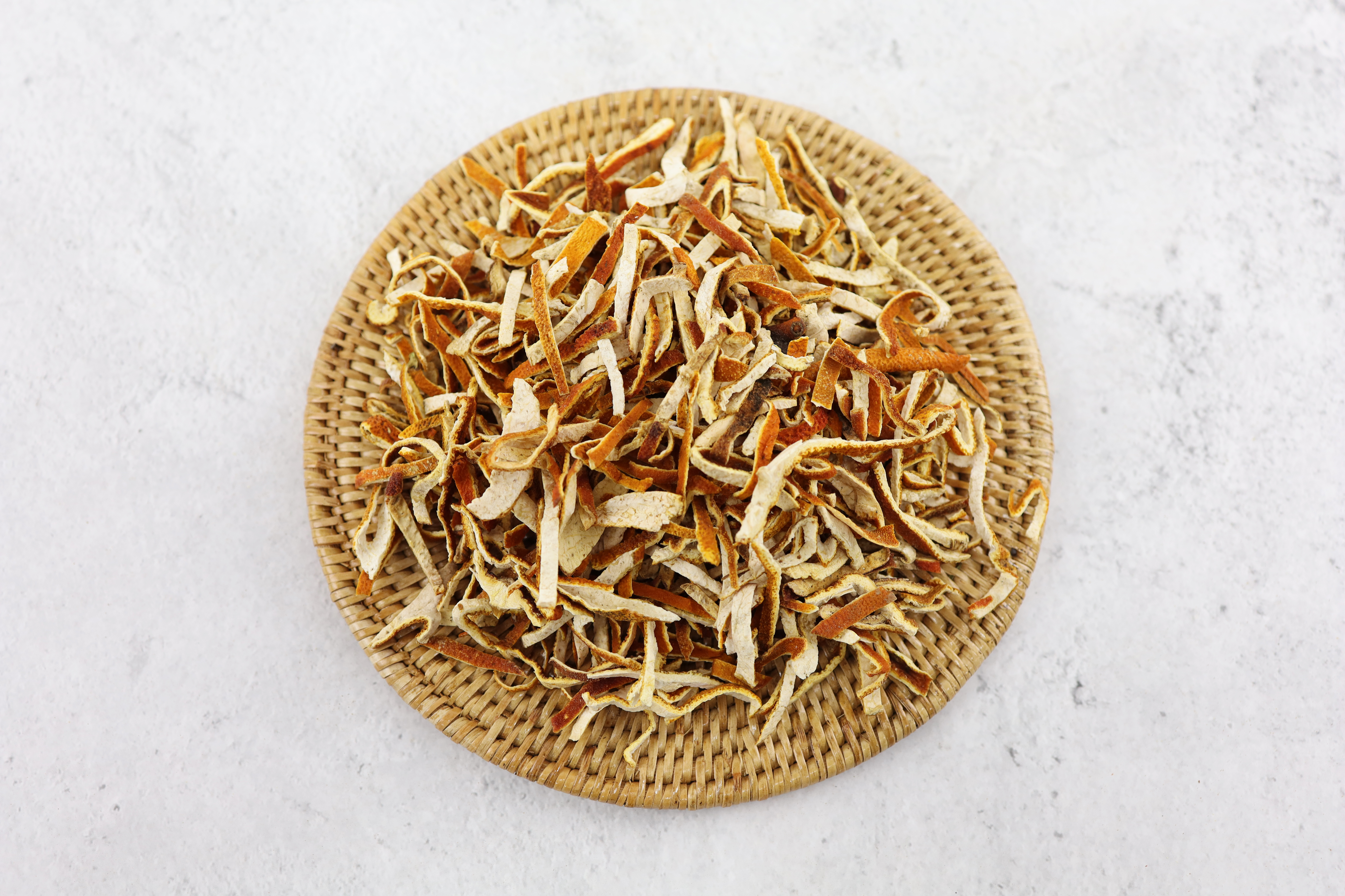 야생의 귤나무에서 채취를 한 귤의 껍질을 잘 세척해서 바싹 말린 후에 편으로 잘라서 만든 진피를 하얀 바닥 위에 대나무로 동그랗게 만든 깔판을 깔고 그 위에 수북하게 쌓아 놓고 찍은 사진