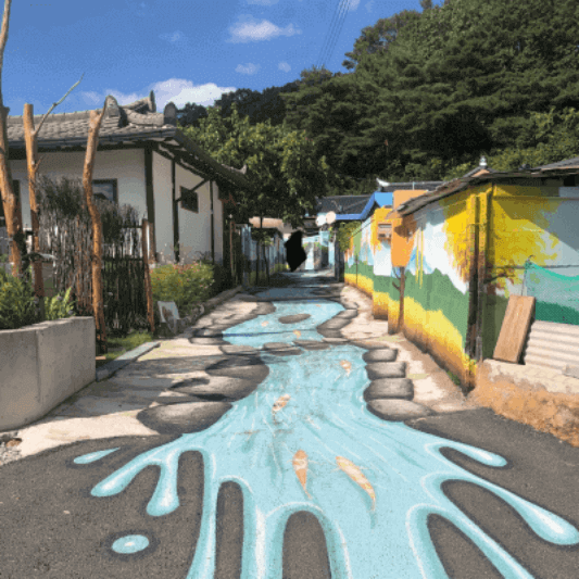 거리가 있고 양옆에 주택이 있다. 그리고 거리와 주택에 벽화가 그려져 있다.
