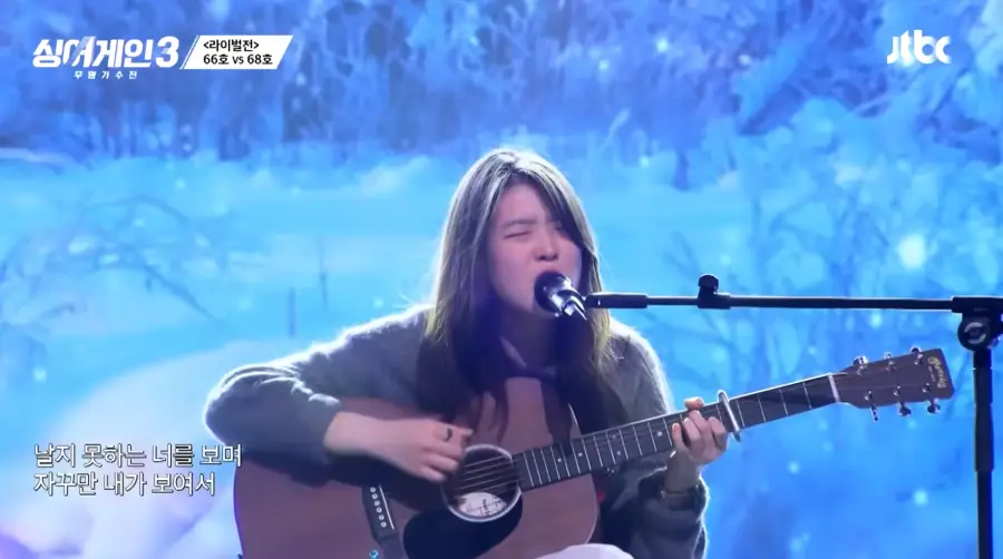 싱어게인3-
갈색기타를 치며 회색 스웨터를 입고 긴머리를 늘어뜨린채 스탠딩마이크 앞에서 노래하는 68호 정면모습