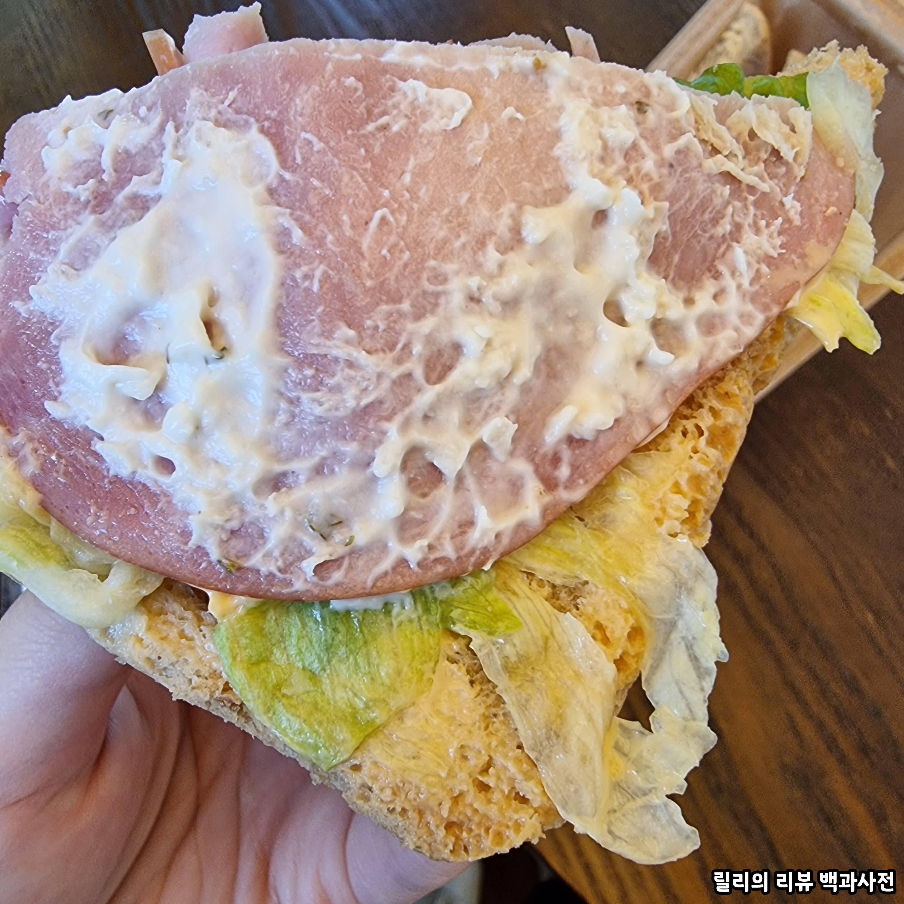 샌드위치 두 빵 중 한 빵을 제거하고 속을 보여주고 있음. 햄에 하얀색 소스가 듬뿍 발려있다.