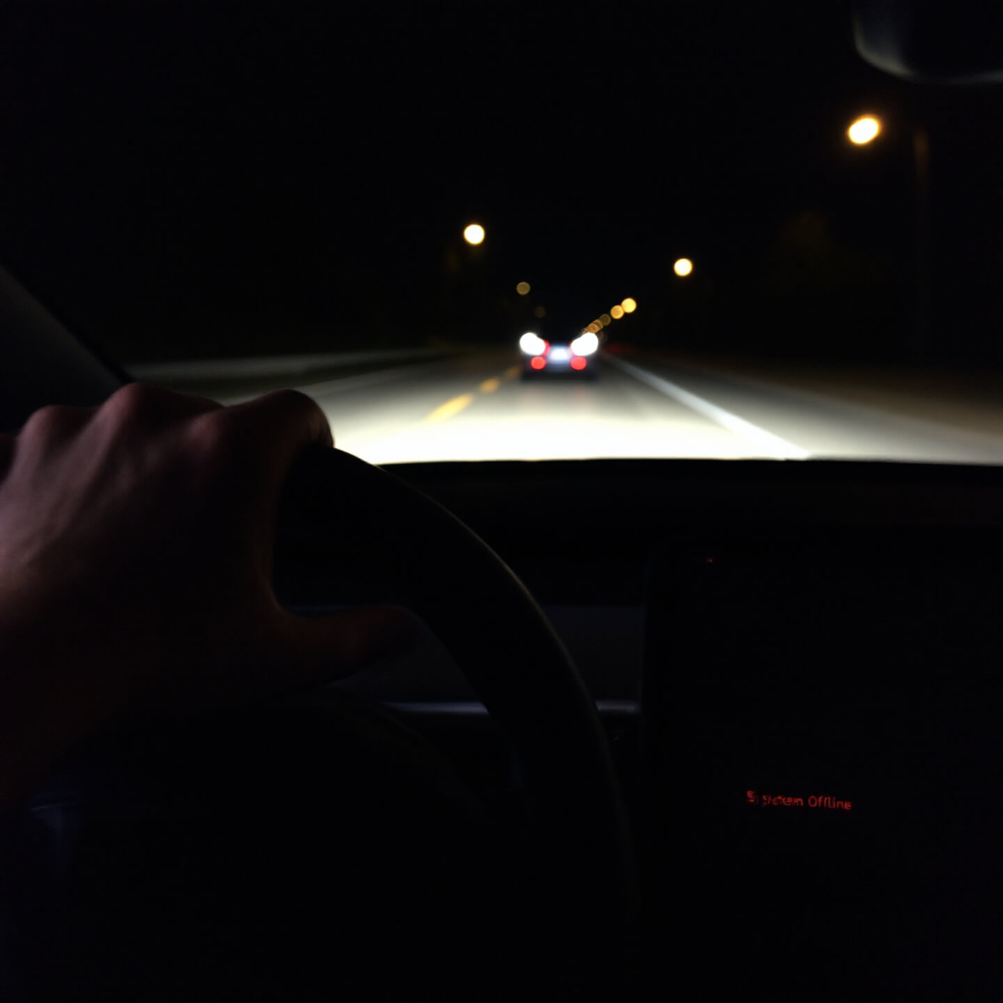 어두운 도로를 주행하는 테슬라 차량 내부에서 운전자가 당황한 채 핸들을 잡고 있음. 차량 디스플레이 화면에 "System Offline" 경고 메시지가 붉은색으로 표시되어 위험한 상황을 나타냄.