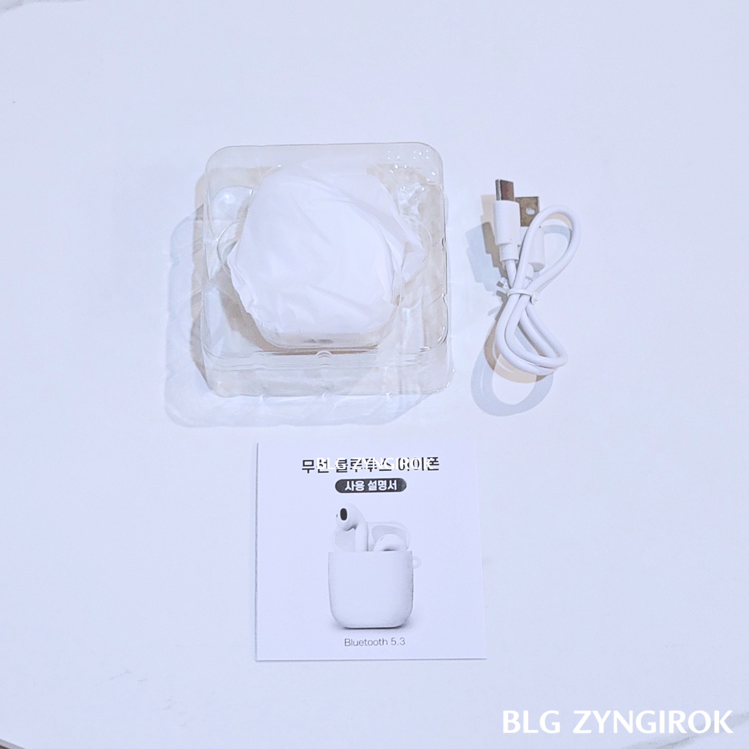 다이소 무선 블루투스 이어폰 구성품인 본체, 충전케이블, 설명서가 테이블 위에 놓여있는 모습이다.
