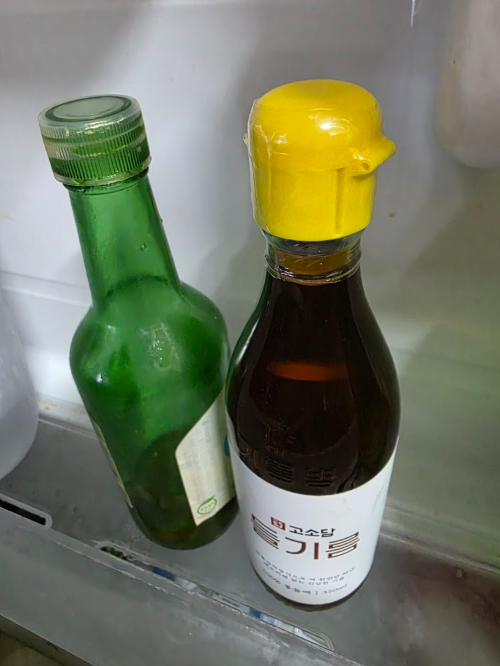 냉장고 문짝 선반 소스 칸에 나란히 보관 중인 초록병 참기름과 노란 뚜껑 들기름 병