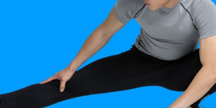 하지근육경련 예방을 위한 스트레칭 동작을 취하는 남성의 모습, 다리를 넓게 벌려 근육을 이완하는 장면.