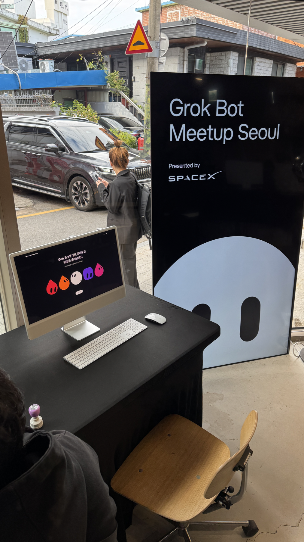 입구 데스크의 iMac 퀴즈 화면과 Grok Bot Meetup Seoul 세로 안내판