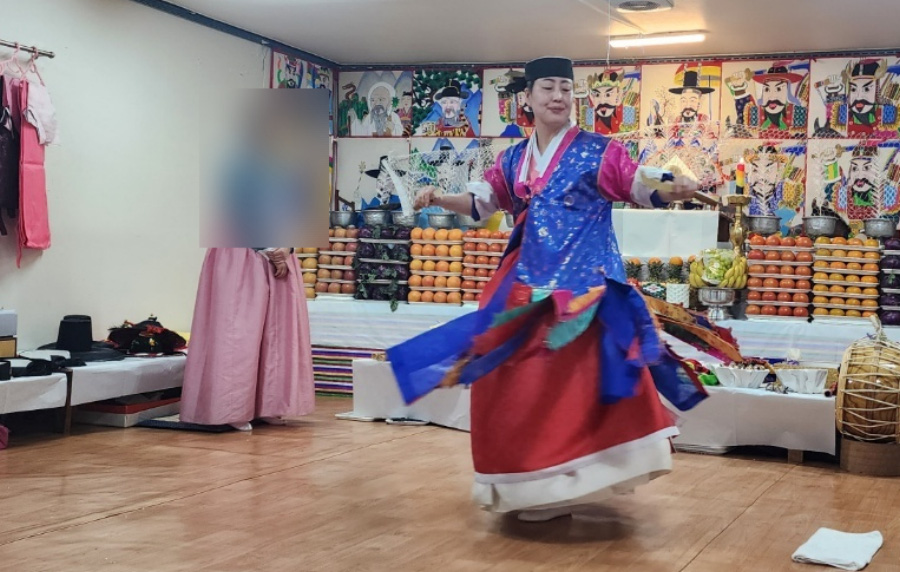 여러 장군들 사진을 그린 그림을 벽에 붙인 굿당에서 음식을 가득 놓아두고 무당이 굿을 벌이고 있는 것을 찍은 사진