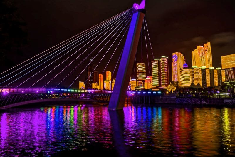 형형색색 조명으로 물든 칭다오의 다리와 야경 속 고층 빌딩이 강물에 반사되어 화려하게 빛나는 장면