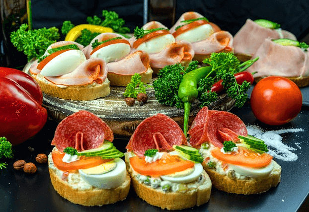 많은 음식들이 있다. 여러개의 바게트빵 조각 위에 햄과 오이, 갊은 달걀 등이 올려졌다.