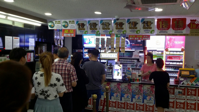 많은 사람들이 줄 서서 로또를 구매하는 복권 판매점의 활기찬 모습. '1등 당첨'이라는 문구가 보이며 희망찬 분위기가 느껴진다.