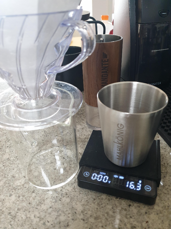 테이블 위에 그라인더, 원두, 서버 그리고 드리퍼가 놓여있다.