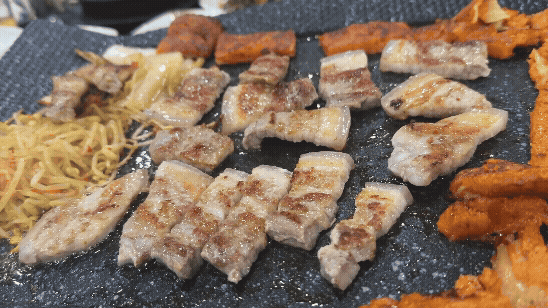 제주산 오겹살이 불판 위에서 한입 크기로 잘라져 노릇하게 구워지고 있는 장면.