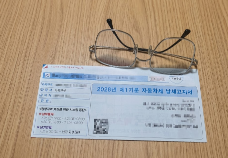 나무 테이블 위에 놓인 2026년 제1기분 자동차세 납세고지서와 그 위의 안경