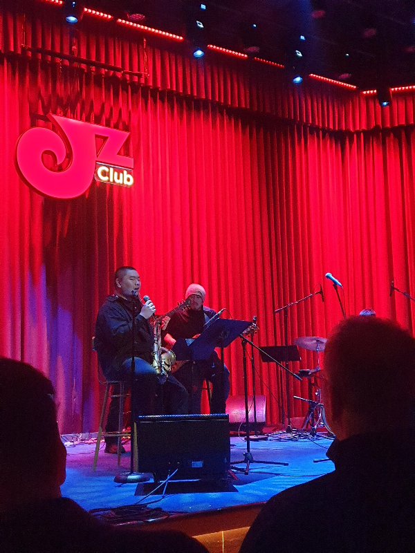 색스폰 주자와 기타리스트가 공연을 하고 있다. 보이지는 않지만 피아니스트와 드러머도 있다.