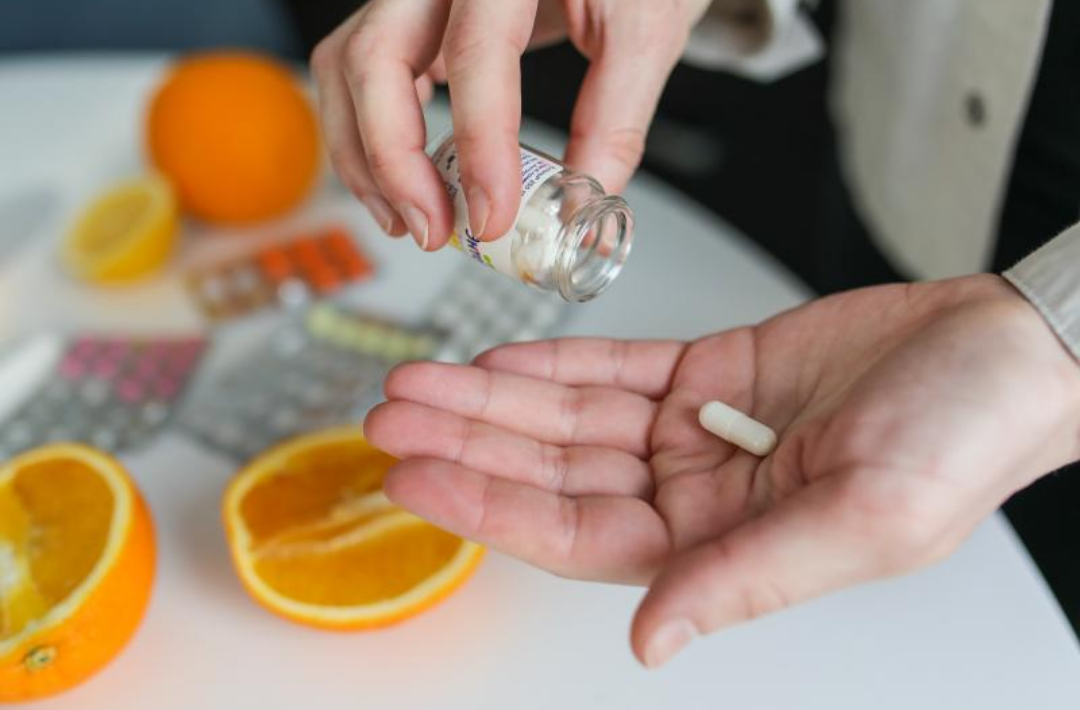 주위에 오렌지가 있고 한 손에 비타민 영양제가 있다.