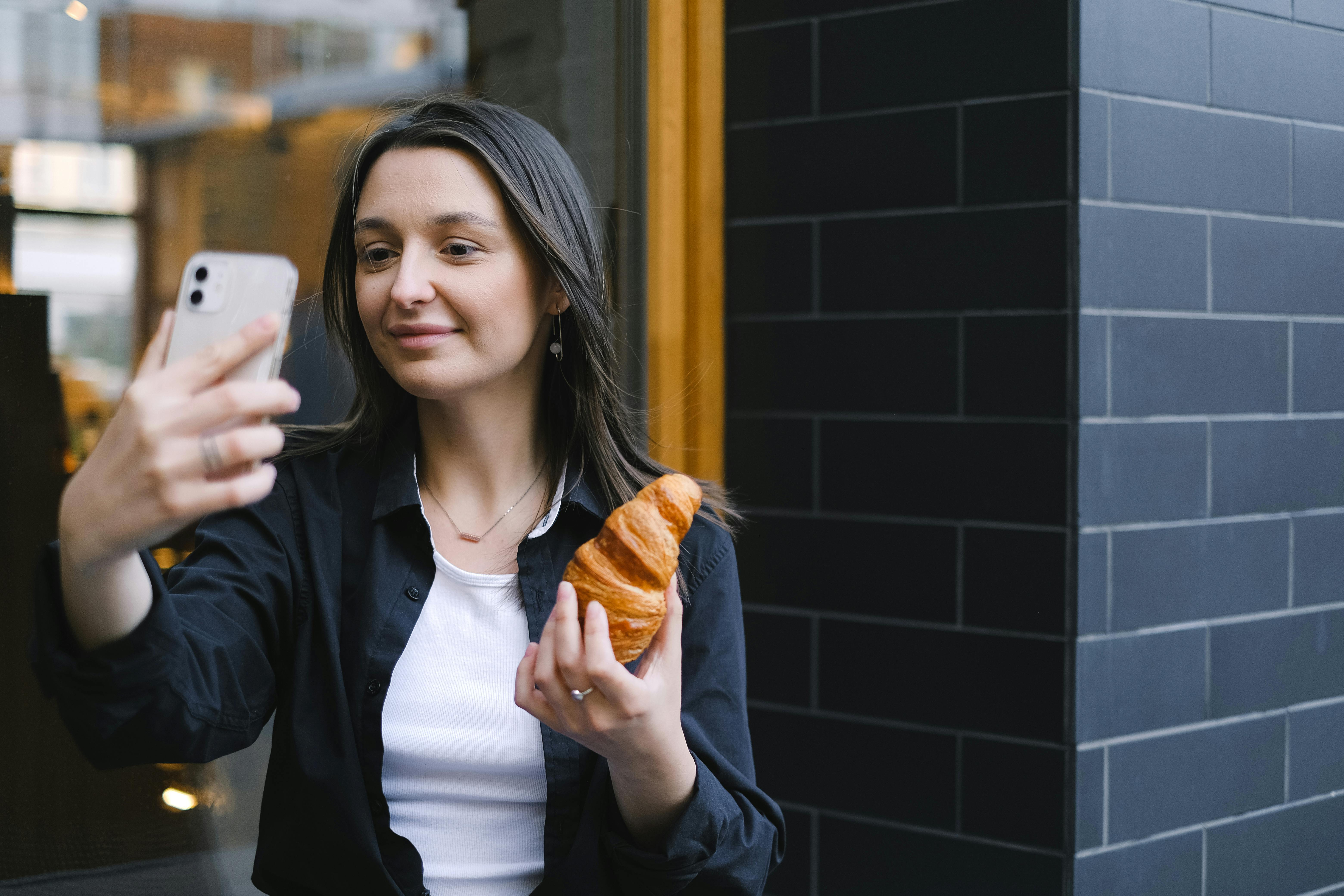 왼손에 빵을 들고, 오른손으로 빵을 든 자신의 모습을 촬영하는 여자