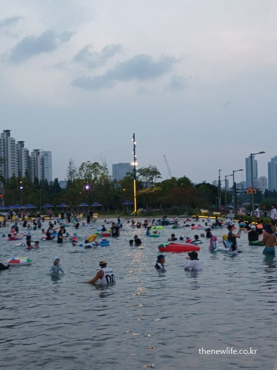 도심 고층 건물들을 배경으로 잠실 한강공원 물놀이장에서 여유롭게 물놀이를 즐기는 시민들