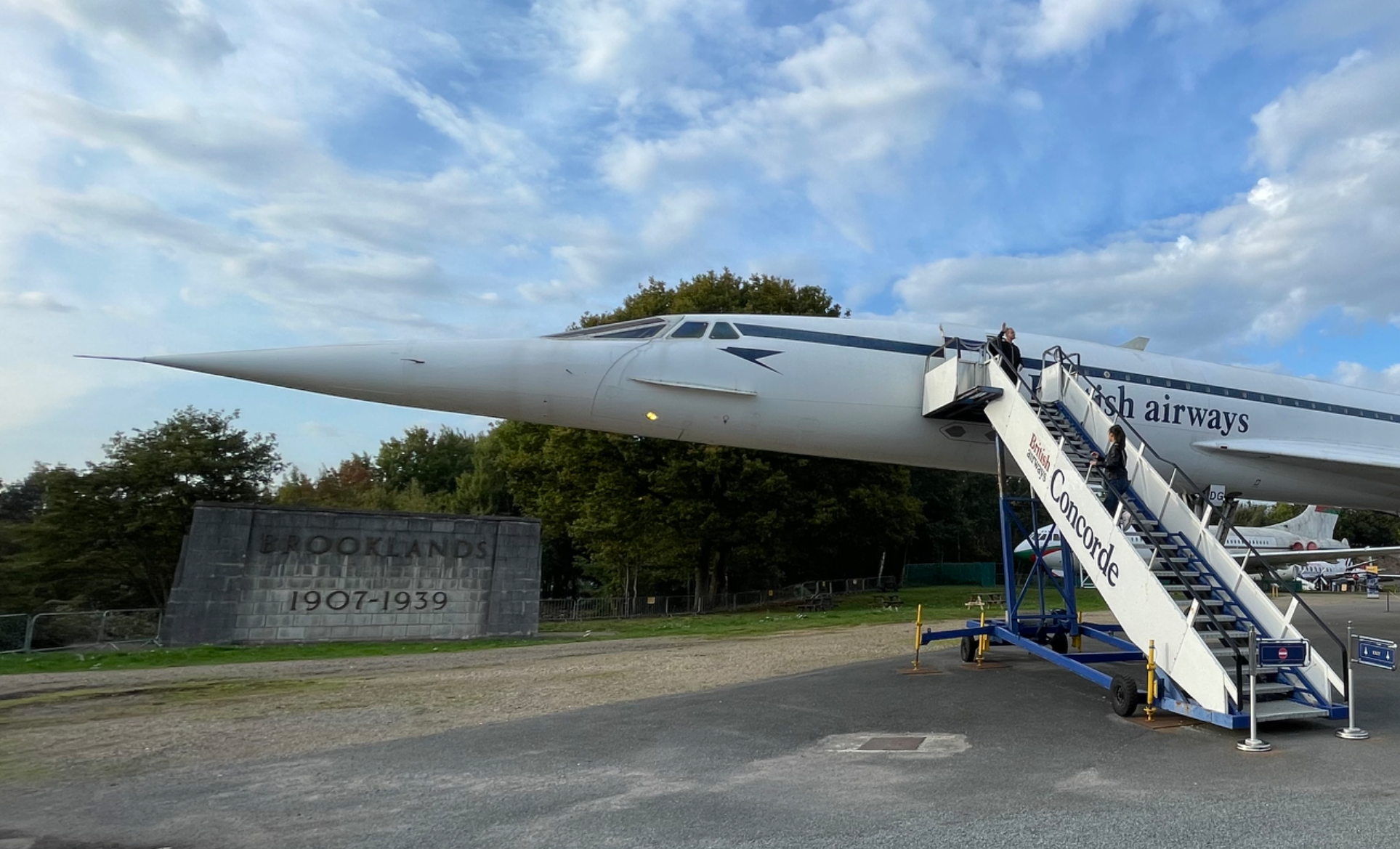 브루클랜즈 박물관 야외에 전시된 콩코드 여객기와 관람객들이 탑승 계단을 오르는 모습. British Airways 로고가 보이며, 배경에는 ‘BROOKLANDS 1907-1939’ 석조 기념비도 함께 있다.