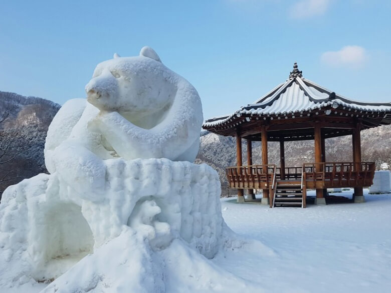 정자를 뒤로하고 눈으로 만들어진 거대한 곰의 형상을한 눈조각품