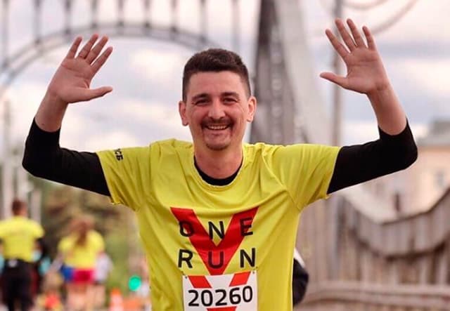 모스크바 국제 마라톤에 참가한 아르템 알리스케로프가 검정색 긴팔 티를 입은 위에 넘버가 적힌 노란색 반팔 티 경기복을 걸쳐 입은 모습으로 양팔을 어깨 높이로 들고 활짝 웃고 있는 모습, 뒤로는 다른 참가자들의 모습이 희미하게 보인다