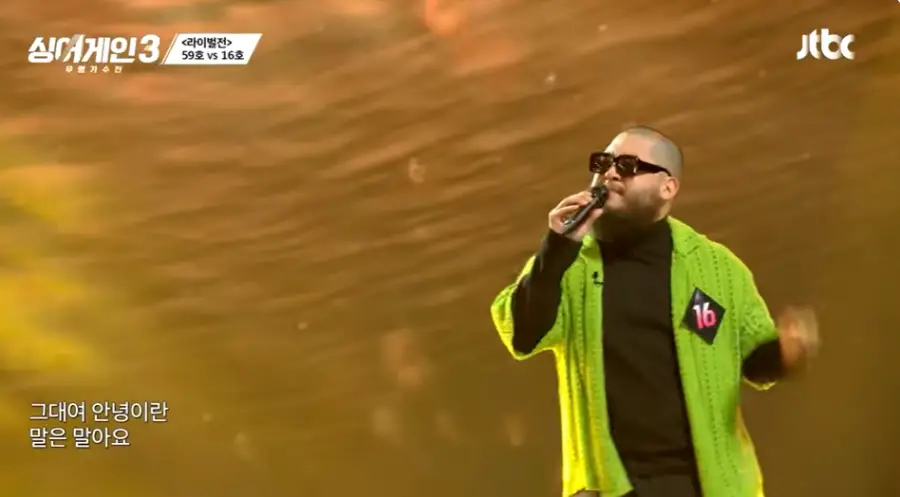 싱어게인3-
황금색배경 연두색 스웨터 안 검은 폴로티를 입고 검은선글라스에 검은 마이크를 입에대고 노래하는 16의 왼쪽 옆모습