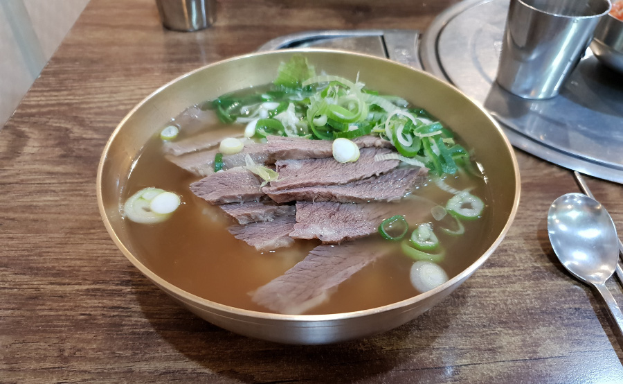 식당에서 파는 소고기 뭇국을 테이블 위에 놓아두고 옆에는 숟가락, 젓가락을 놓아두고 찍은 사진