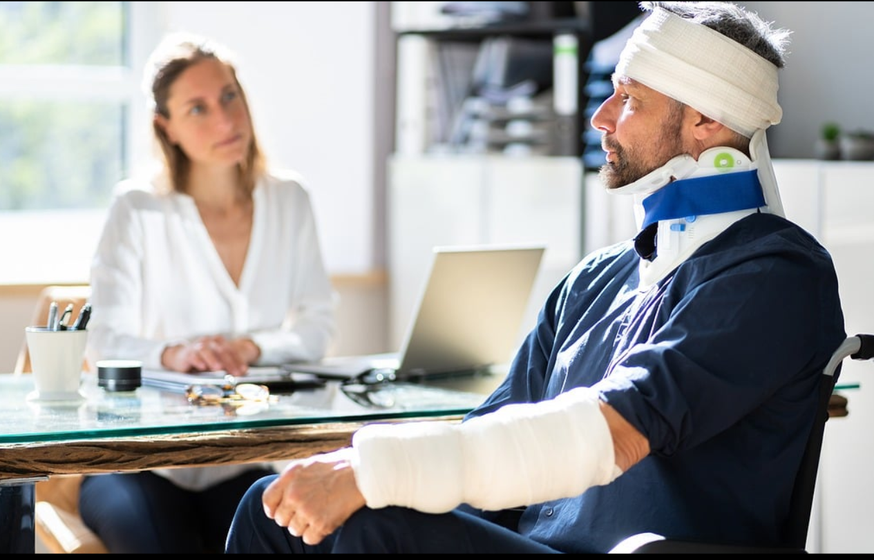 한 남자가 목과 팔에 깁스를 하고 휠체어에 앉아서 여성의사와 상담하는 사진