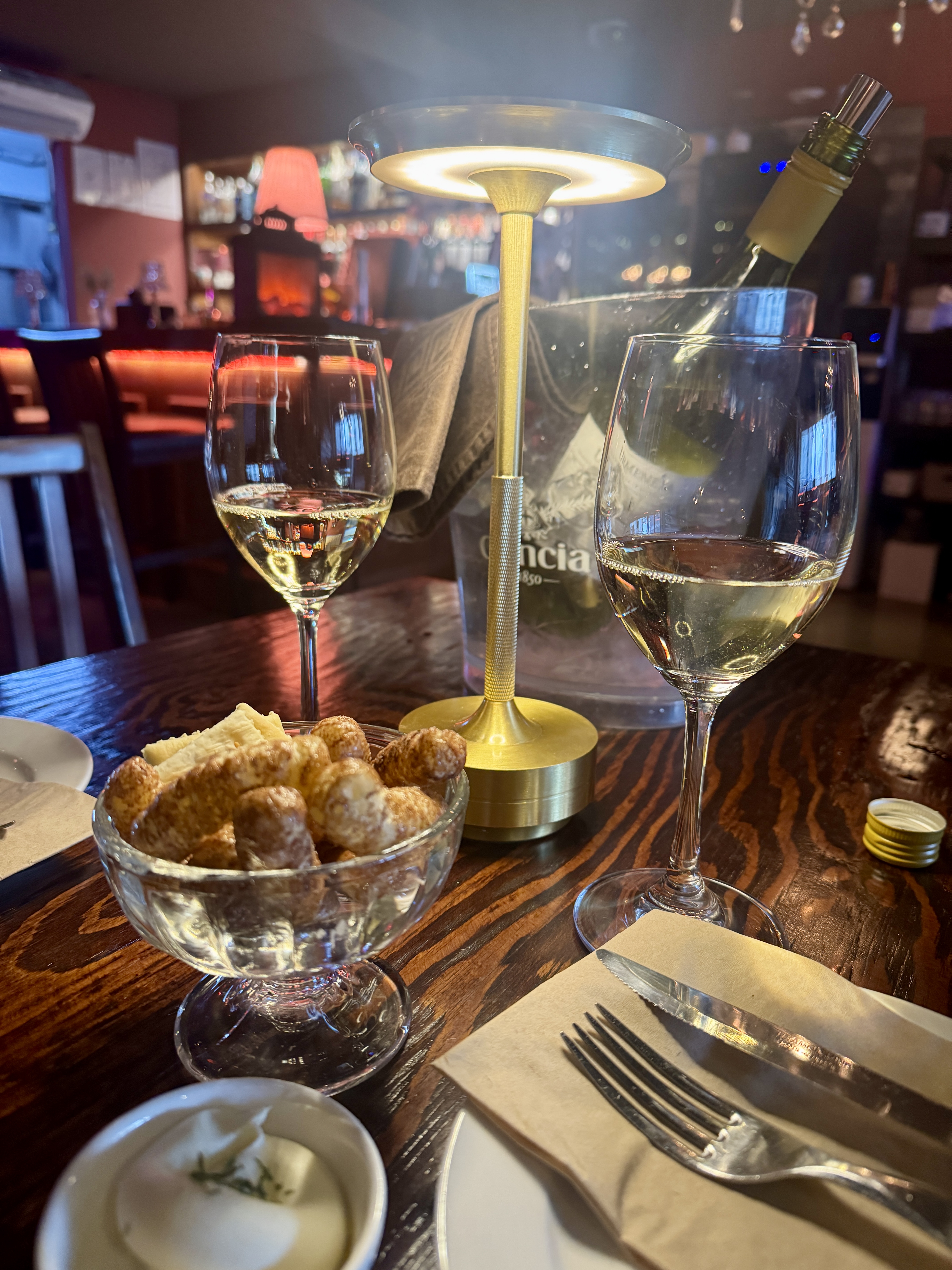 논현동 와인바 테이블 위 와인잔 두 개와 와인 버킷&amp;#44; 스낵이 놓여 있고&amp;#44; 아늑한 조명 아래 따뜻한 분위기가 느껴지는 모습.