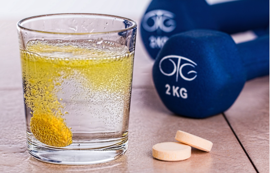 청소년기 영양 결핍이 미치는 심리적 영향 (우울, 불안, 피로), 컵에 발포비타민이 녹고 있으며 옆에는 2 kg의 아령이 있는 사진