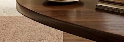 따뜻한 베이지 톤의 미니멀한 실내 공간과 통유리창 너머 푸른 정원이 조화를 이루는 브랜드 플래그십 스토어의 전경입니다. 원목 테이블 위의 커피 한 잔과 세련된 계단 구조가 여유롭고 지적인 라이프스타일의 분위기를 자아냅니다.