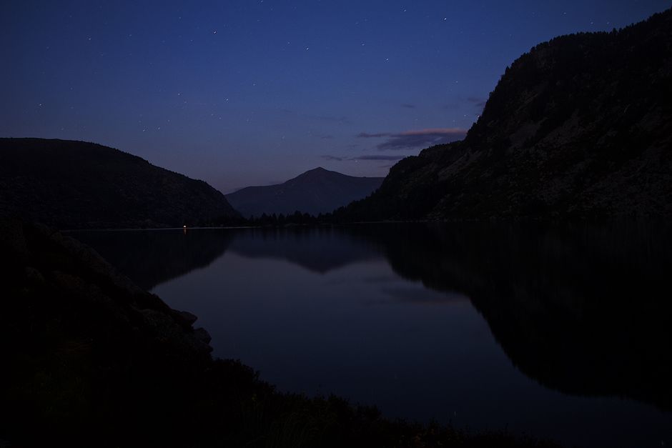 Stunning night reflection of mountains on a tranquil lake, under a starry sky.