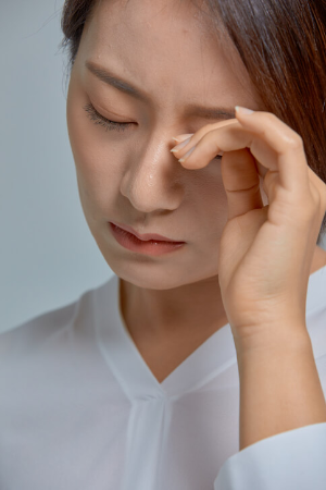 눈이 피로한 듯 눈 부위에 손을 올리고 있는 여성
