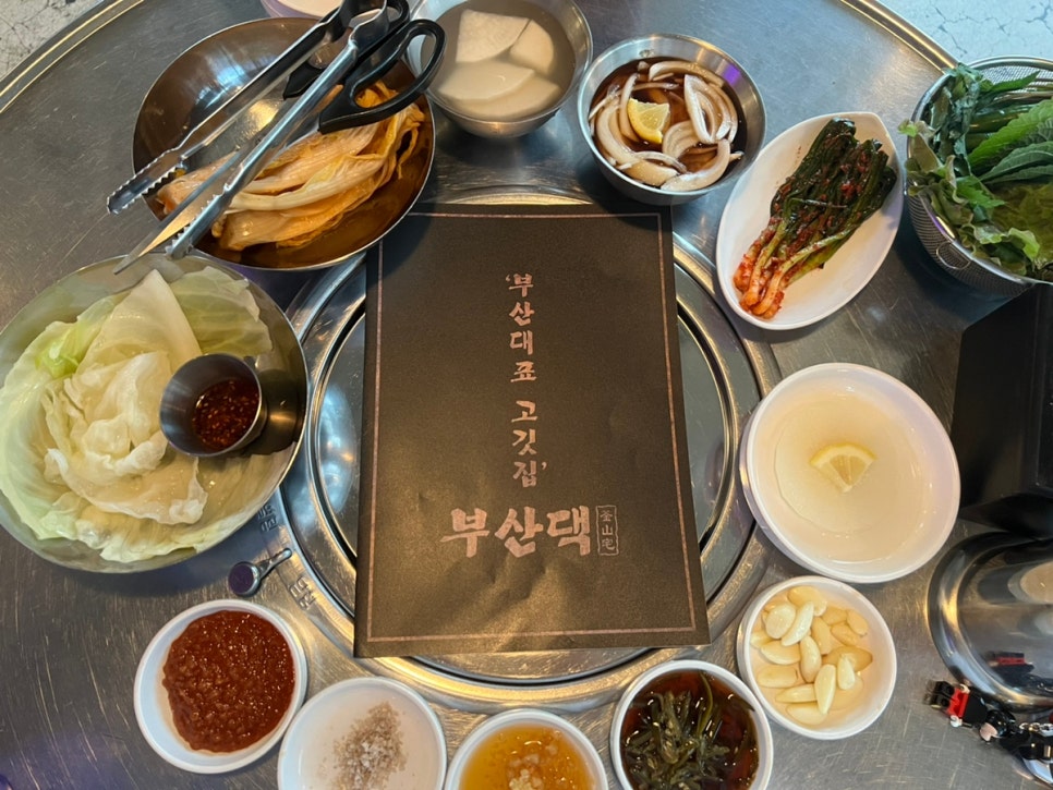 기장 삼겹살 맛집 부산댁에서 제공되는 다양한 밑반찬 한 상 차림, 신선한 야채와 반찬들이 정갈하게 놓인 모습