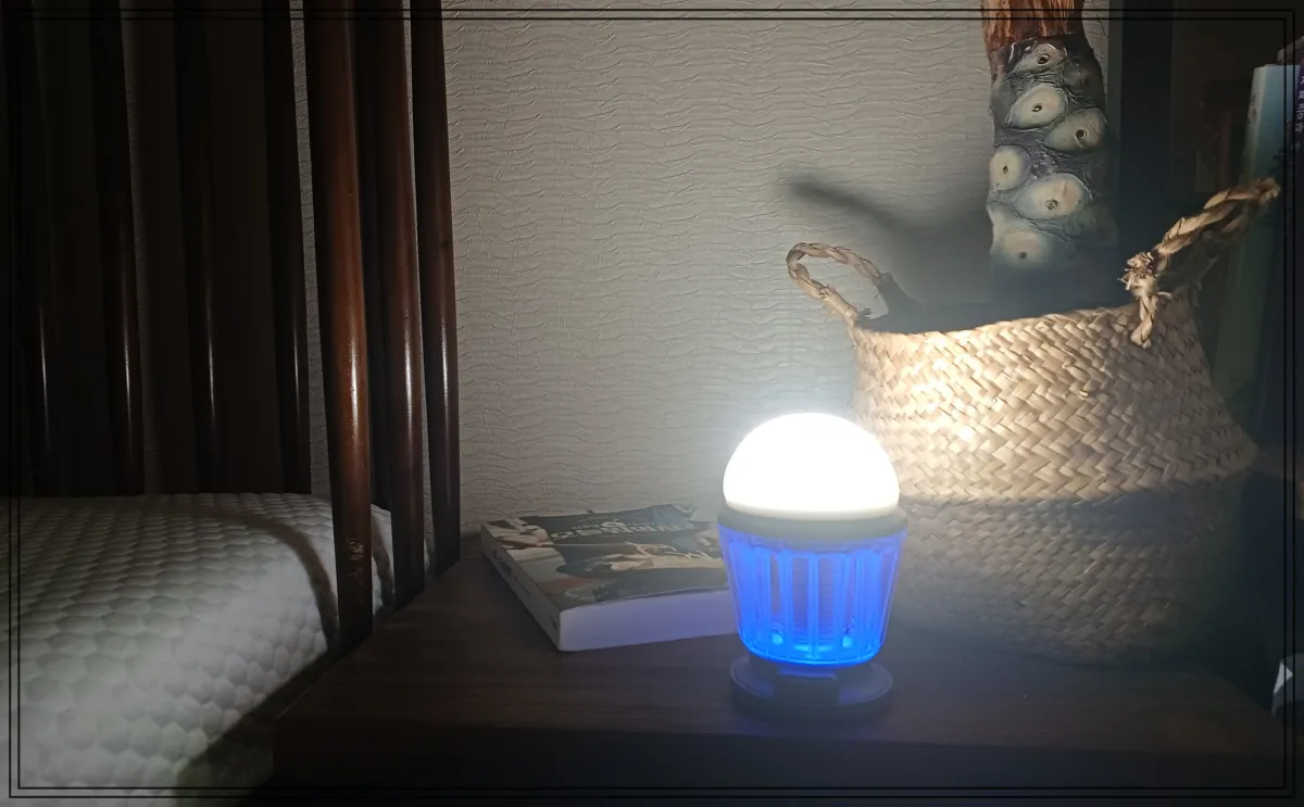 침대-옆-협탁에-놓인-하와스-캠핑랜턴이-켜진-상태로-주변을-은은하게-비추고-있으며-책과-라탄-바구니-소품이-함께-보인다