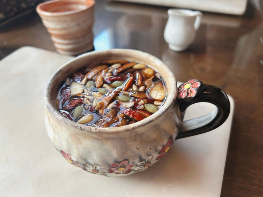 갈색의 테이블 위에 꽃무늬가 있는 전통 찻잔 세트에 대추와 호두, 잣 등이 들어 있는 쌍화차를 가득 담아두고 찍은 사진