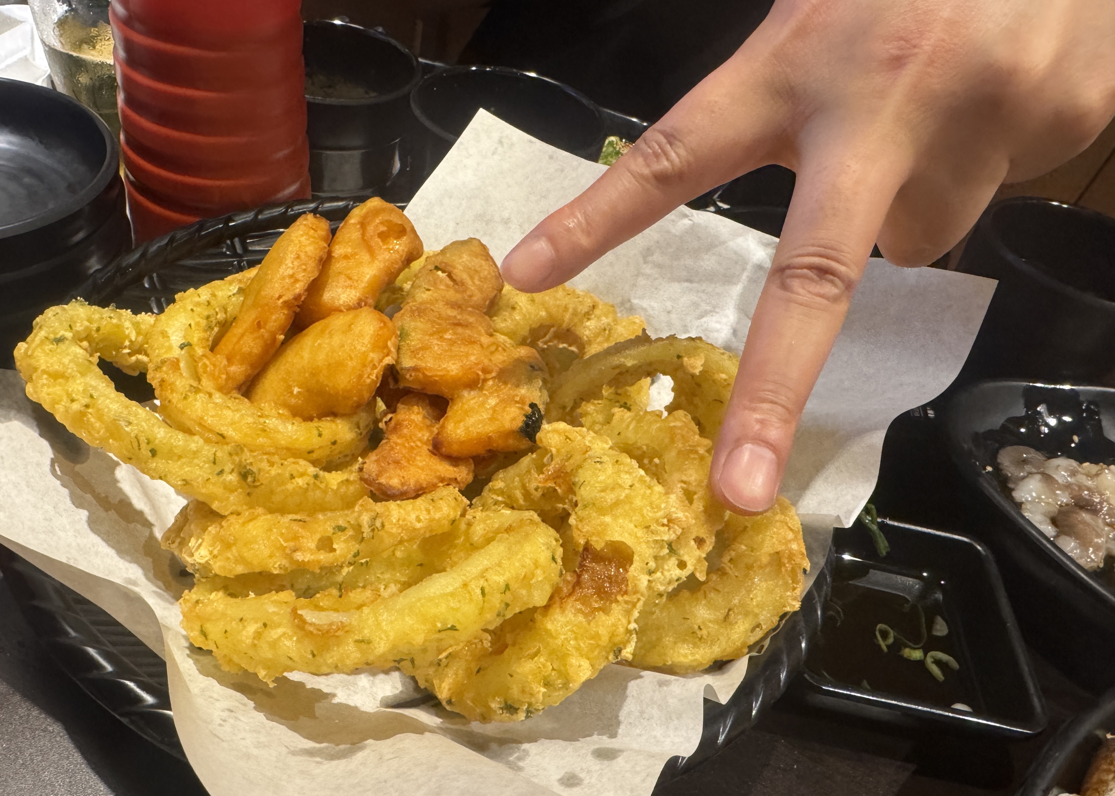 물고기 자리 논현점에서 제공된 튀김 요리. 바삭하게 튀겨진 양파링과 고구마튀김이 바구니에 담겨 있고&amp;#44; 한 손이 브이 포즈를 하고 있다.