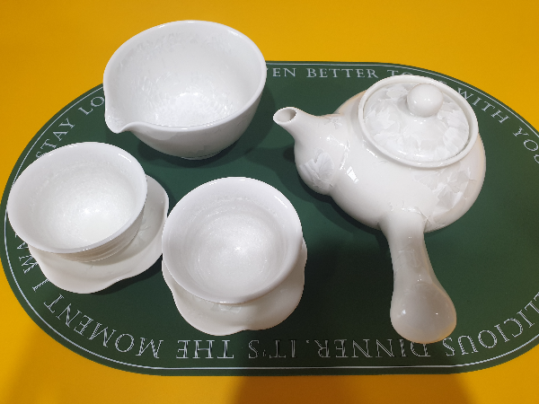 노란색 탁자 위 헌터색 테이블 매트가 있다. 매트 위 위에 다도 세트가 있다. 앞쪽 찻잔 2개와 위쪽 공도배 그리고 오른쪽 다관이 보인다.