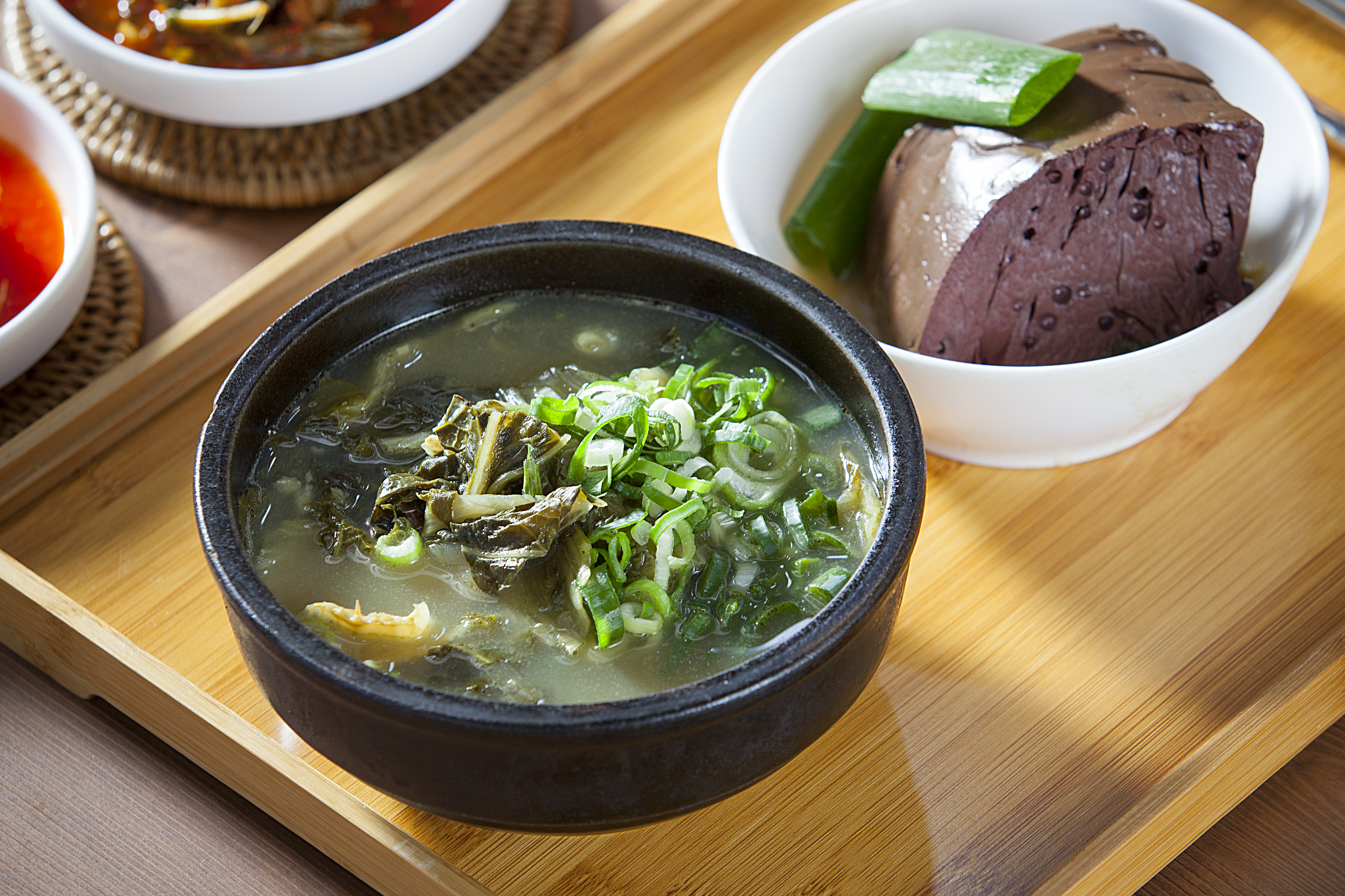 네모난 나무쟁반 위에&#44; 검은 뚝배기에 우거지를 넣고 끓인 우거지해장국을 가득 담아놓은 것을 두었고&#44; 그 옆에는 하얗고 동그란 사기 그릇에 소의 피를 응고하여 삶은 선지를 가득 담아 놓은 것을 위에서 찍은 사진