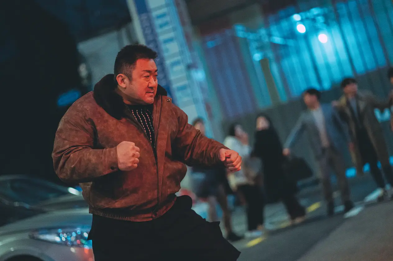범죄도시-갈색 점퍼 검은바지를 입고 두 주먹을 불끈 쥔 마동석