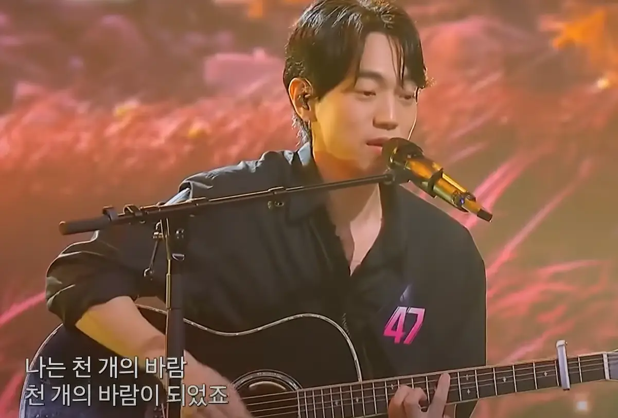 싱어게인3- 검은색 셔츠와 청바지에 가슴에 47번호표를 달고 검은색 기타를 치며 스탠딩마이크를 앞에 두고 앉아 노래하는 47호