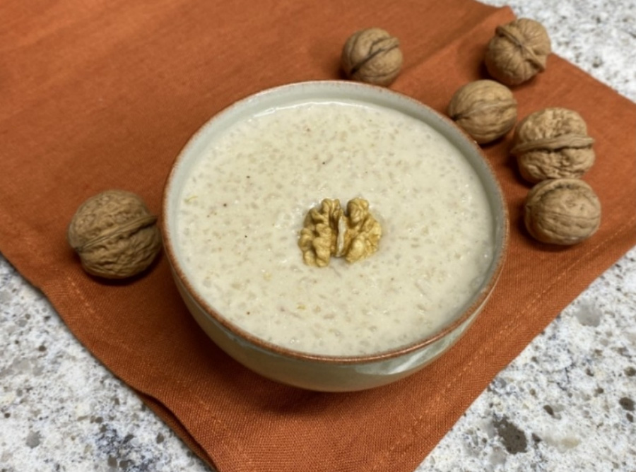 야생에서 채취를 한 호두를 믹서로 잘 갈아서 찹쌀과 함께 쑨 호두죽을 담은 동그란 그릇을 대리석 바닥 위에 주황색 깔판을 깔고 그 위에 호두 4개와 함께 놓고 찍은 사진