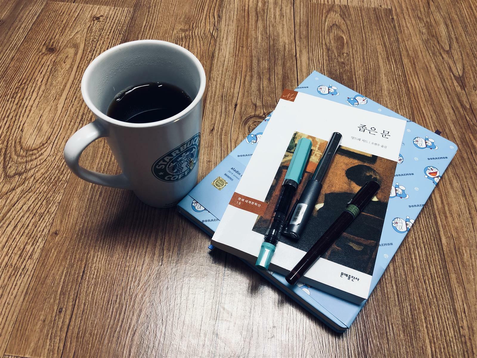 커피한잔과 좁은문 책과 메모노트 그리고 만년필 3개가 놓여진 사진입니다