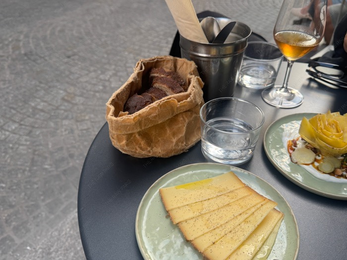 French small plates with sliced Comté cheese, artichoke dish, and fresh sourdough bread in a paper bag