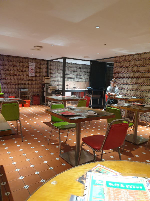 오렌지 브라운의 흰 다이아 패턴 바닥 타일과 벽면 반복 패턴을 가진 홀. 직원이 앉아 있다.