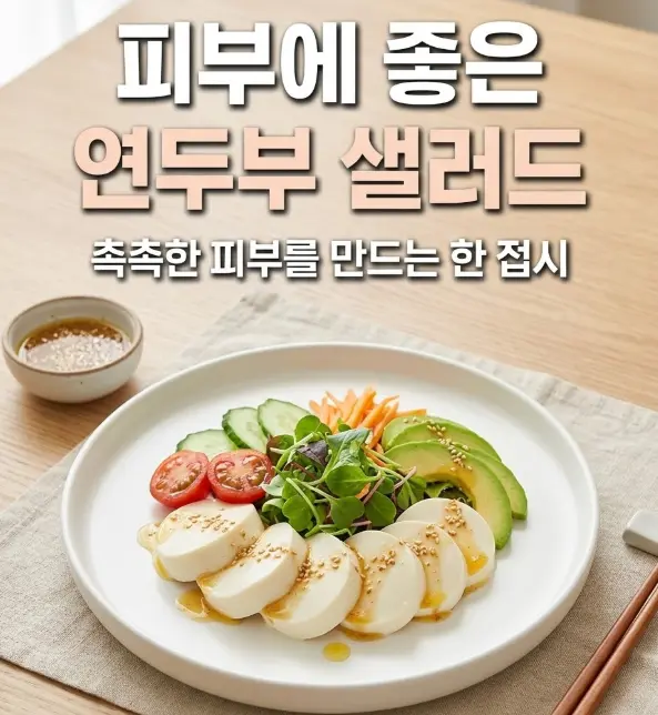 흰 도자기 접시 위에 부드러운 연두부와 방울토마토, 오이, 아보카도, 어린잎 채소가 올려진 샐러드에 참깨 간장 드레싱이 뿌려진 밝고 깨끗한 테이블 세팅