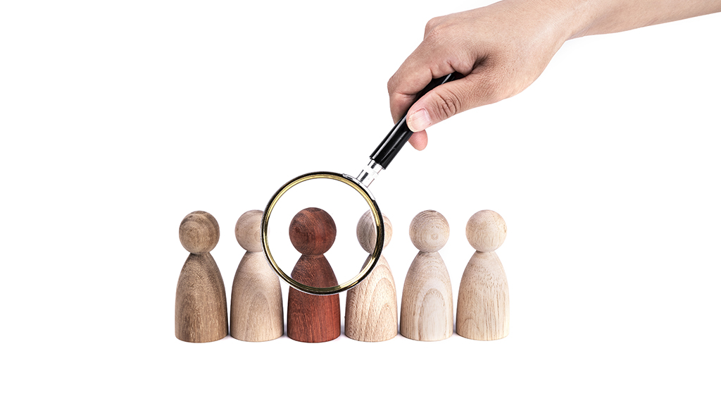 여섯 개의 나무 인형이 줄지어 있고 그 중 세번째 인형이 돋보기로 관찰되는 모습