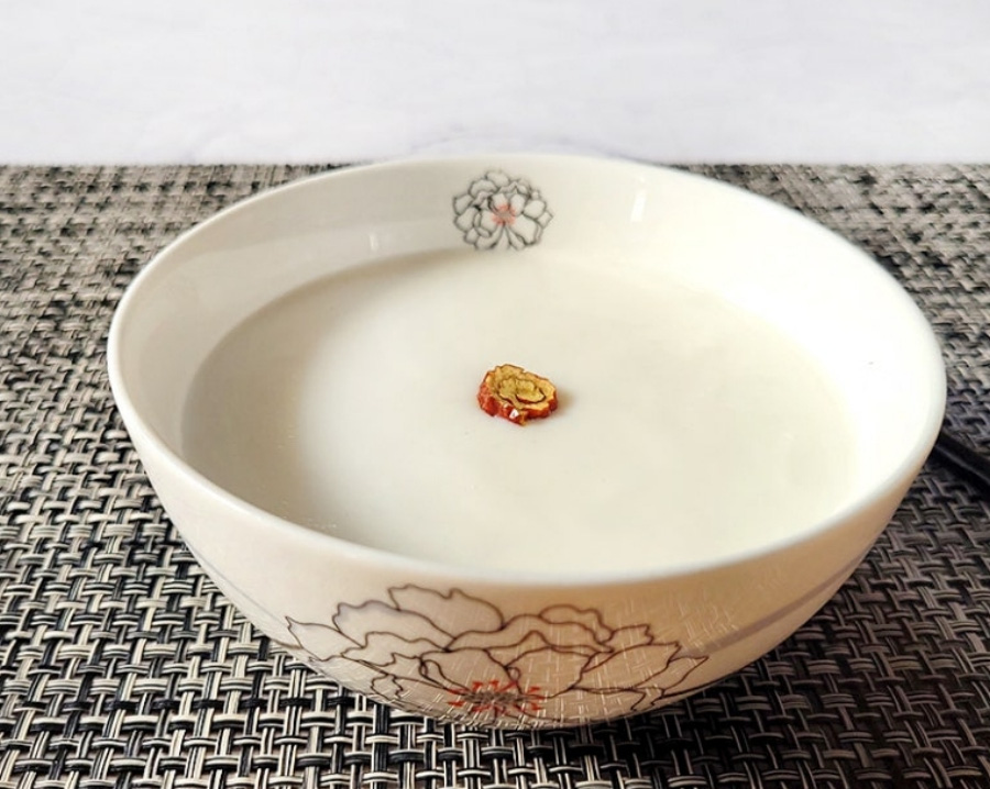 쌀을 갈은 후에 우유와 함께 넣어서 끓인 우유죽을 동그랗고 하얀 그릇에 가득 담아두고 대추 조각을 위에 올려 놓은 것을 대나무로 만든 검은 바닥 위에 놓아두고 찍은 사진