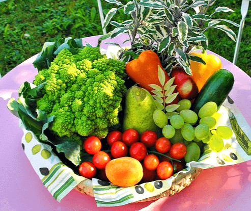 야외 식탁 위에 야채가 가득하다. 녹색 콜라비, 주황색 파프리카, 오이, 청포도, 방울토아토가 가득하다.