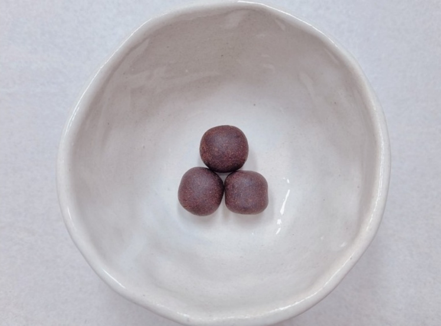 하얀 바닥 위에 동그랗고 하얀 그릇을 놓아두고, 그 속에 한약을 갈아서 꿀과 함께 버무려서 만든 청심환 크기의 환약 3개를 놓아두고 찍은 사진