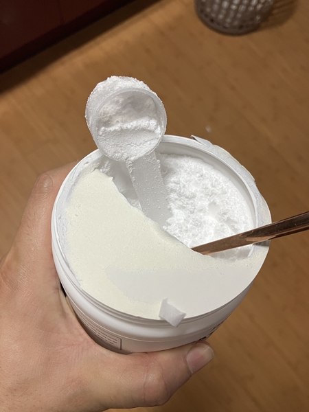 뉴트리코스트 크레아틴 용기 속 긴 손잡이 계량 스푼과 하얀 파우더&amp;#44; 옆에 젓가락이 놓인 모습